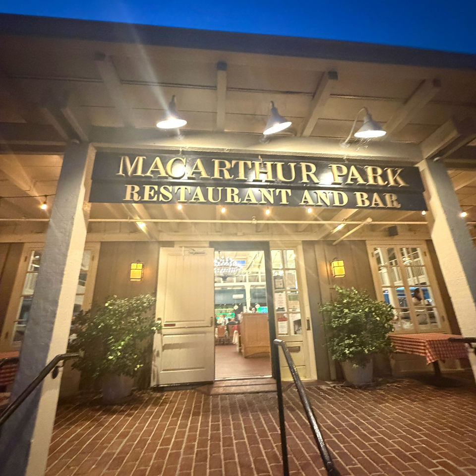 Exterior entrance of MacArthur Park Restaurant and Bar, warmly lit beneath a covered porch with potted shrubs and brick flooring.