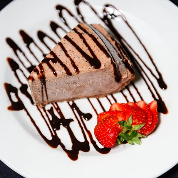 A slice of chocolate ice cream cake drizzled with chocolate sauce, served with fresh strawberries.
