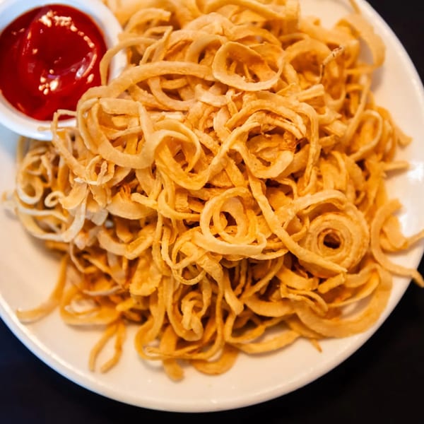 Crispy fried onion strings with a side of bright red ketchup on a white plate.