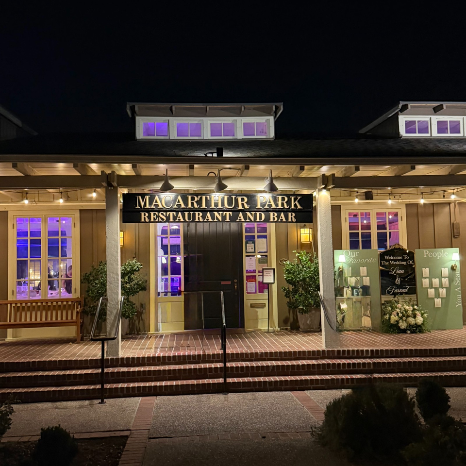 Nighttime exterior of MacArthur Park Restaurant and Bar, with illuminated purple windows, brick steps, plants, and wedding displays.