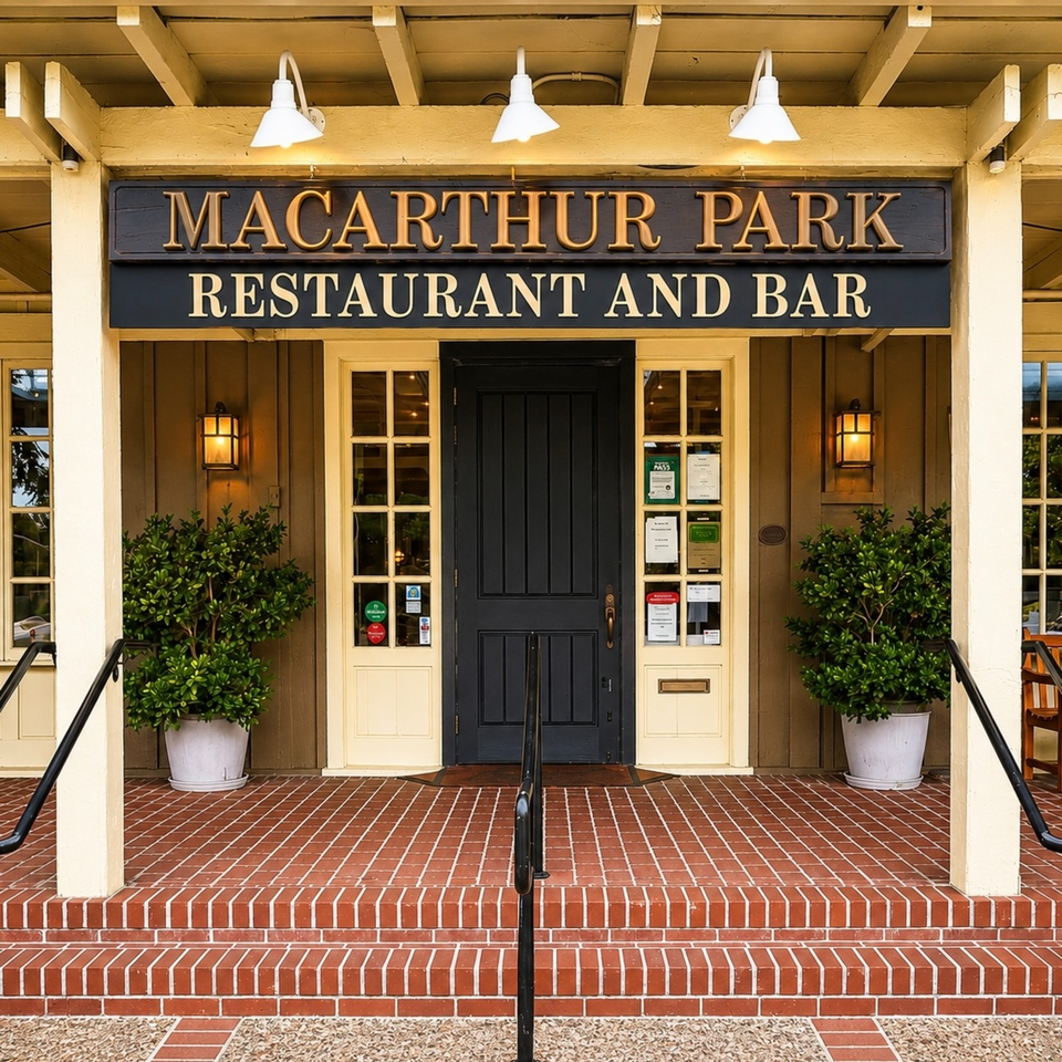 Entrance to MacArthur Park Restaurant and Bar with black door, brick steps, potted shrubs, and illuminated wall lanterns.