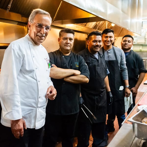 MacArthur Park Restaurant's kitchen staff, including a chef in white, posing in a professional kitchen.