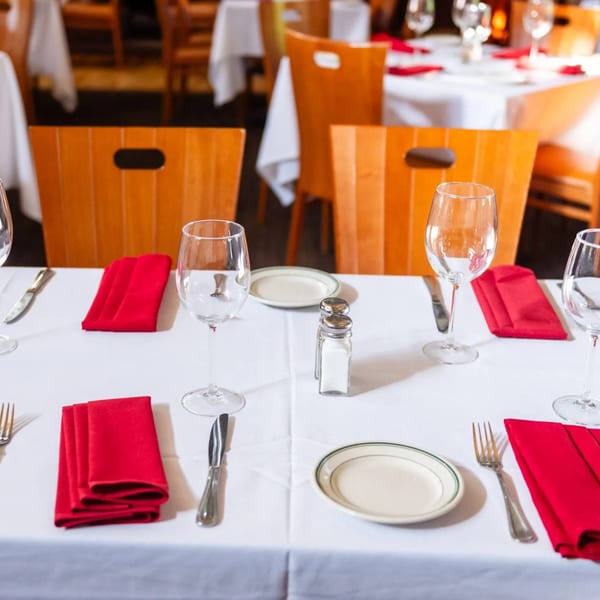 Set tables with white tablecloths, red napkins, wine glasses, and wooden chairs at MacArthur Park Restaurant.
