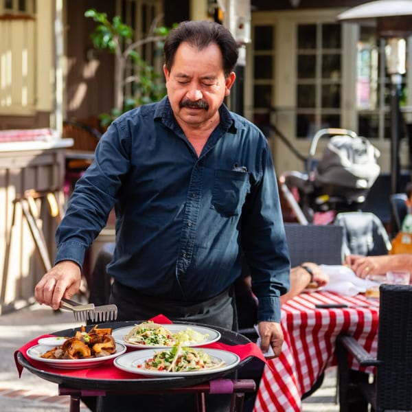 A server at MacArthur Park Restaurant and Bar places plates of food onto a tray outdoors.