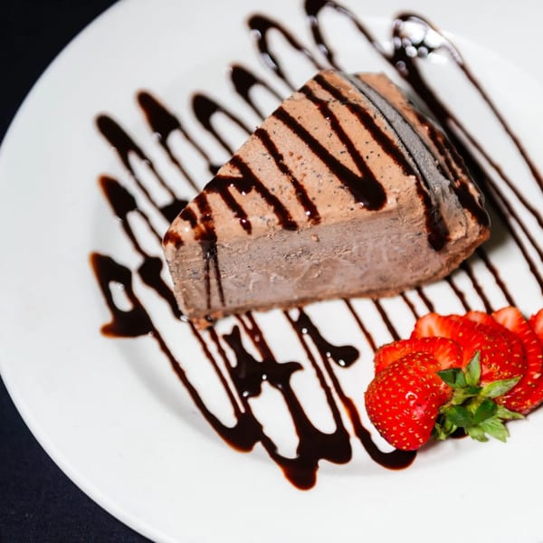 A slice of chocolate ice cream cake with chocolate drizzle and sliced strawberries on a white plate.