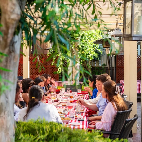 Patrons enjoy an outdoor meal at MacArthur Park Restaurant, seated at a long table with red and white checkered tablecloths.