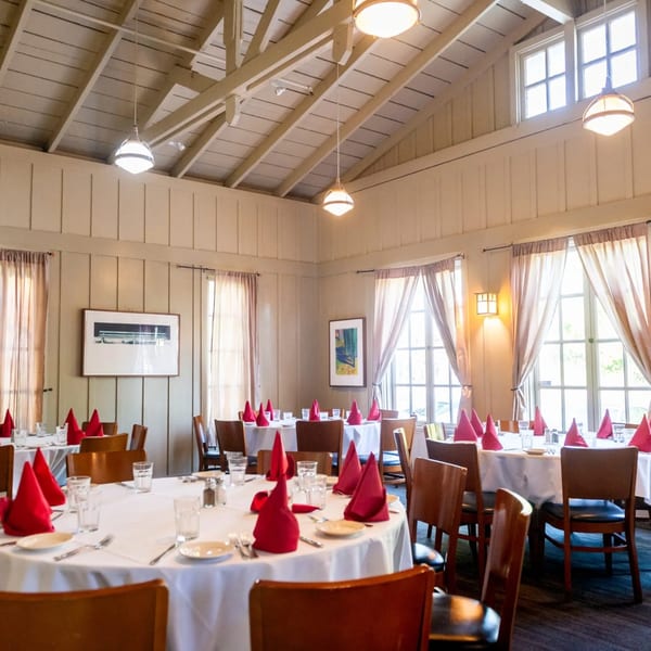 Dining room at MacArthur Park Restaurant with white-clothed tables, red napkins, and large windows.