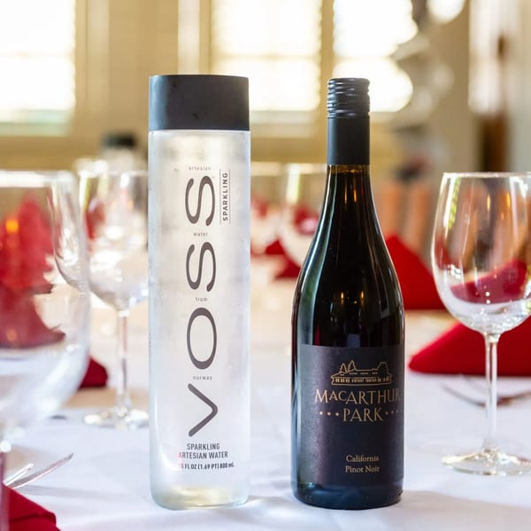 MacArthur Park Pinot Noir and Voss sparkling water on a white tablecloth with red napkins.