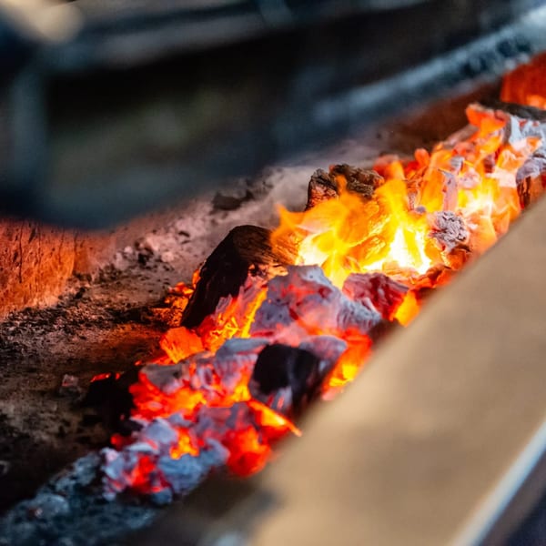 Close-up of glowing embers and flames in a wood-fired grill at MacArthur Park Restaurant.