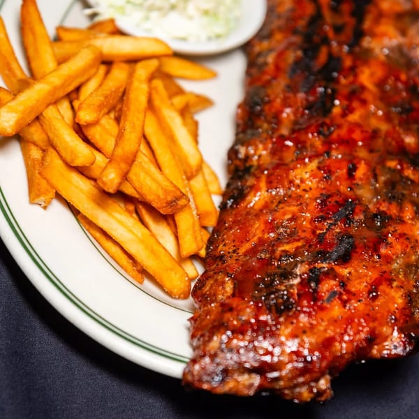 A plate of MacArthur Park Restaurant's BBQ ribs with a side of golden french fries and coleslaw.