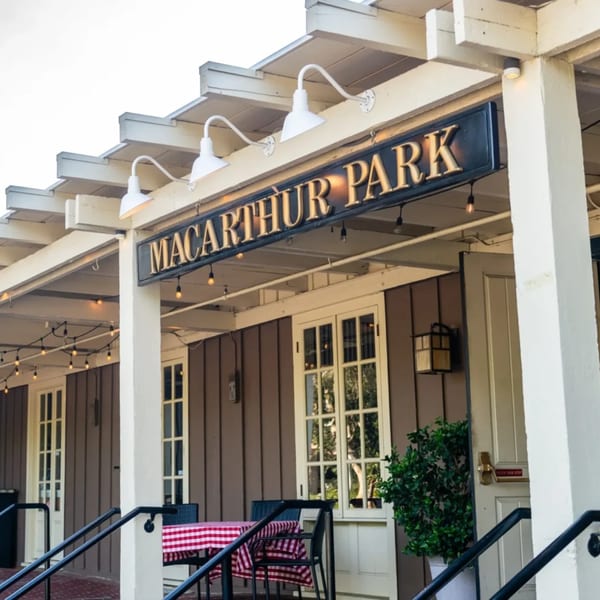 Exterior of MacArthur Park Restaurant with a prominent sign, string lights, and outdoor seating.