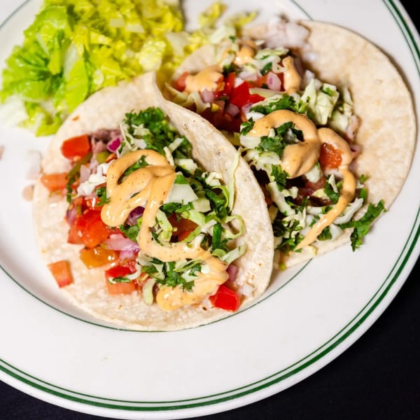 Two MacArthur Park fish tacos with salsa, cabbage, and sauce, served with a side of lettuce.