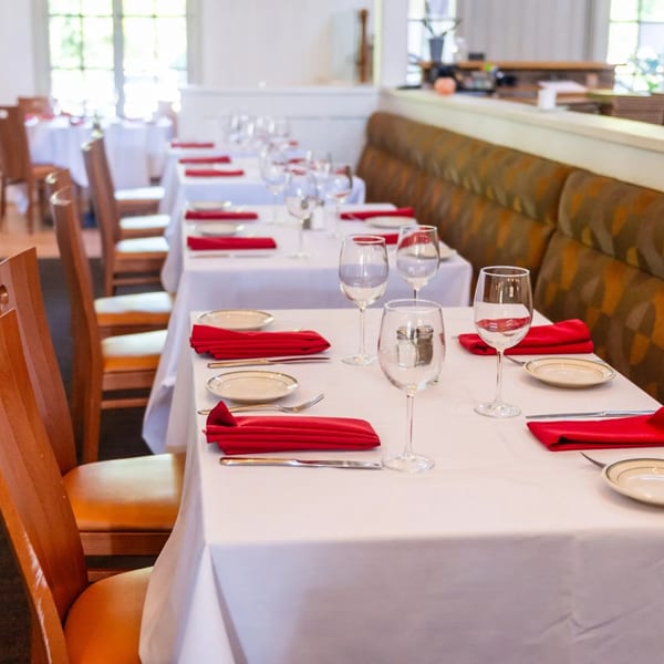 Dining room at MacArthur Park Restaurant with white tablecloths, red napkins, and wooden chairs.