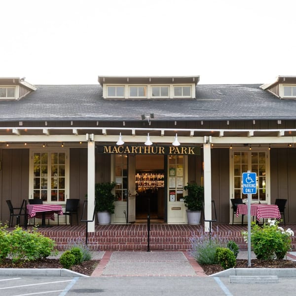 Exterior of MacArthur Park Restaurant, a brown building with a porch, outdoor seating, and a parking lot.