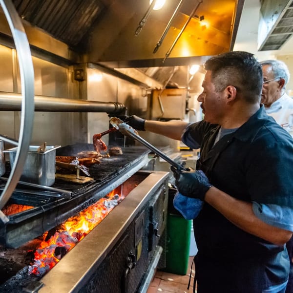 A chef grilling steaks over an open flame in a professional kitchen at MacArthur Park Restaurant.