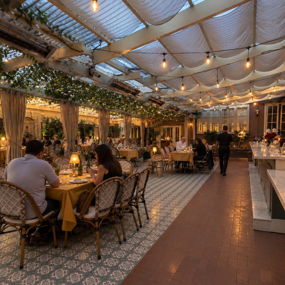 Elegant covered restaurant patio with diners, patterned tile floors, draped ceiling, hanging lights, and lush greenery.