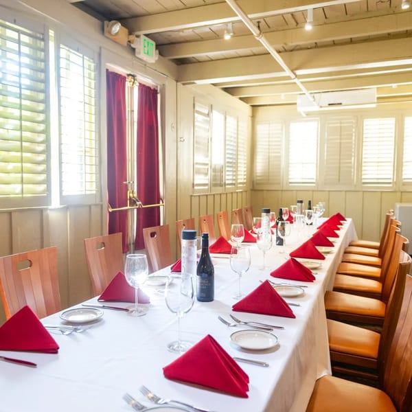 Long dining table set with red napkins, wine glasses, and bottles in a bright room.