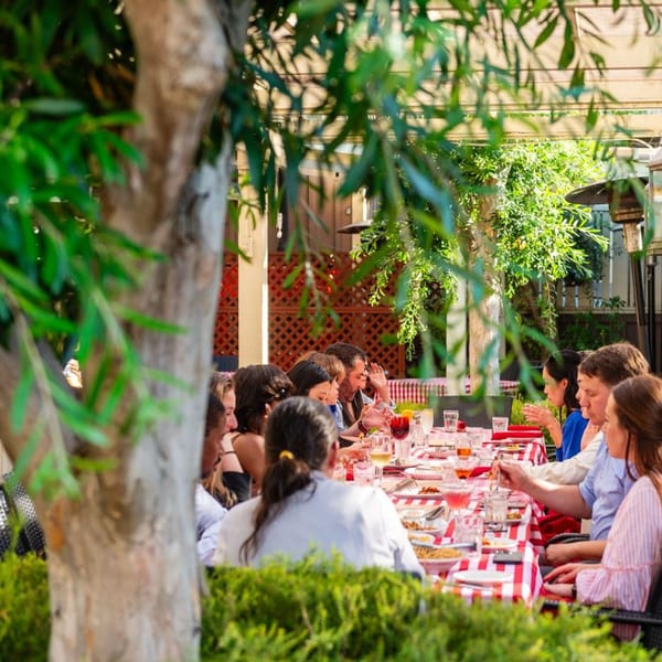 People dining al fresco at a long table with red and white checkered tablecloths.