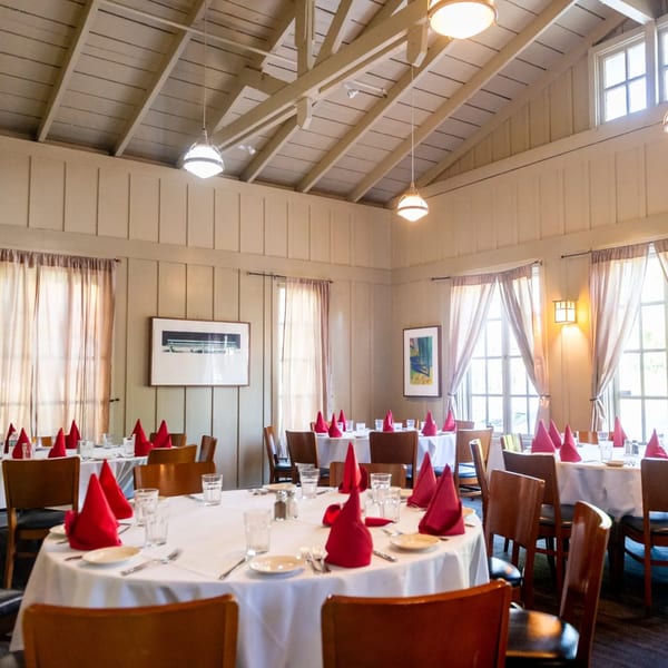 Dining room at MacArthur Park Restaurant with white-clothed tables, red napkins, and wooden chairs under a vaulted ceiling.