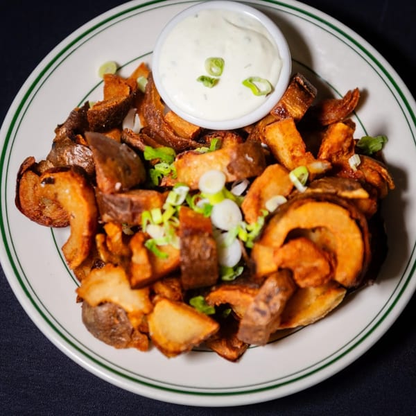 Crispy fried potato wedges with green onions and a side of creamy white dipping sauce.