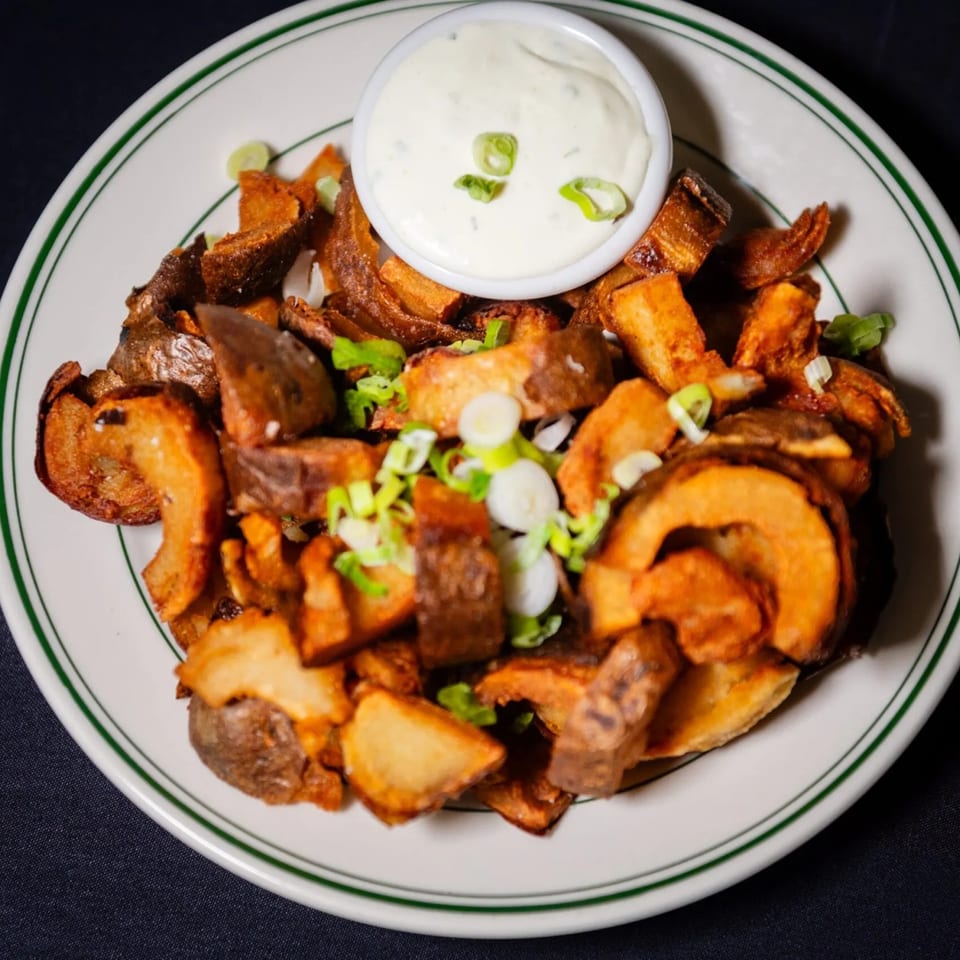 Crispy fried potato wedges with green onions and a side of creamy white dipping sauce.