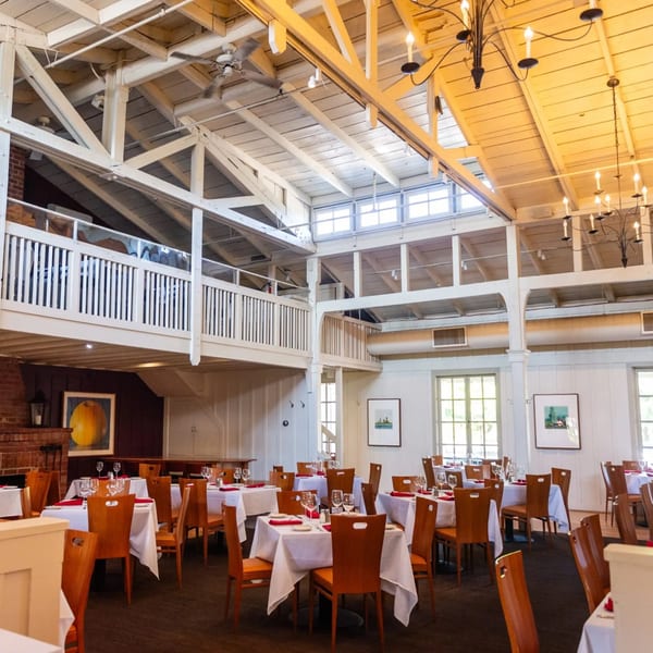 Spacious dining room at MacArthur Park Restaurant with white tablecloths, wooden chairs, and a high vaulted ceiling.