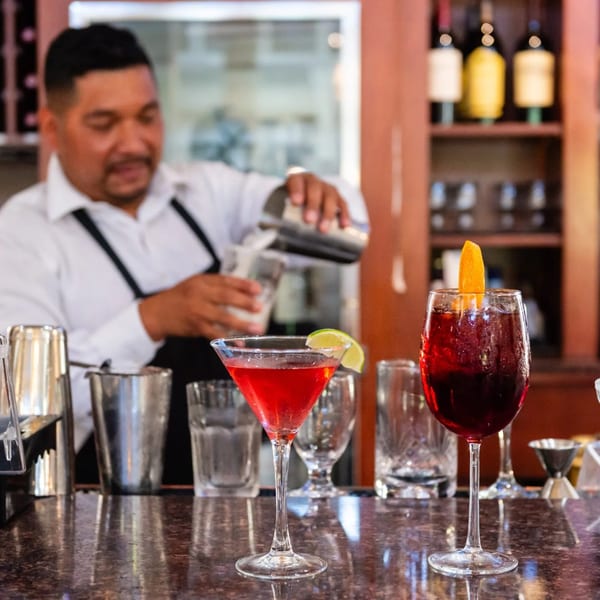 Bartender pouring a drink behind a bar with two cocktails in the foreground at MacArthur Park Restaurant.