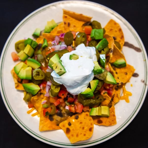 A plate of MacArthur Park Restaurant nachos with cheese, avocado, jalapeños, salsa, and sour cream.