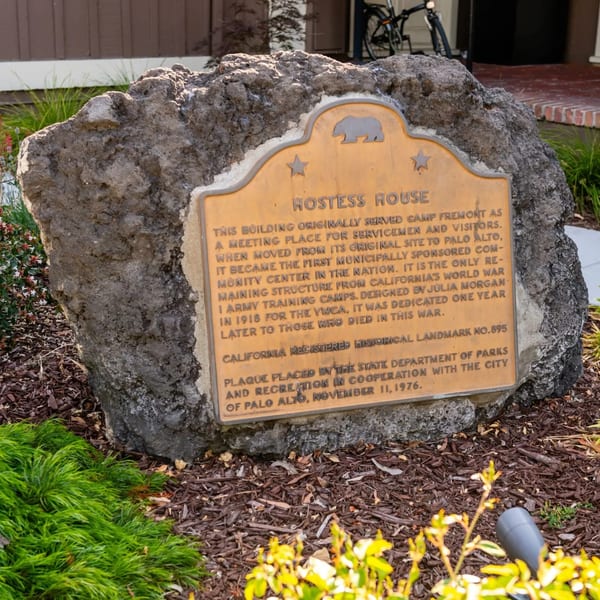 A historical landmark plaque for the Hostess House, set in a large rock with surrounding greenery.
