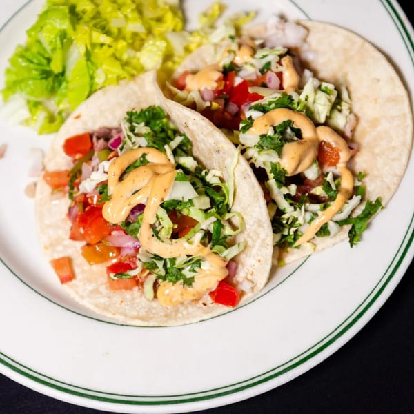 Two American-style tacos with meat, salsa, shredded lettuce, and creamy sauce, served with a side salad.