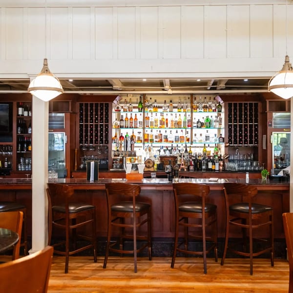 MacArthur Park Restaurant's bar with a wooden counter, bar stools, and shelves filled with liquor bottles.