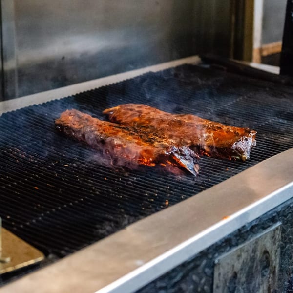 Two racks of ribs cooking on a smoky grill at MacArthur Park Restaurant.