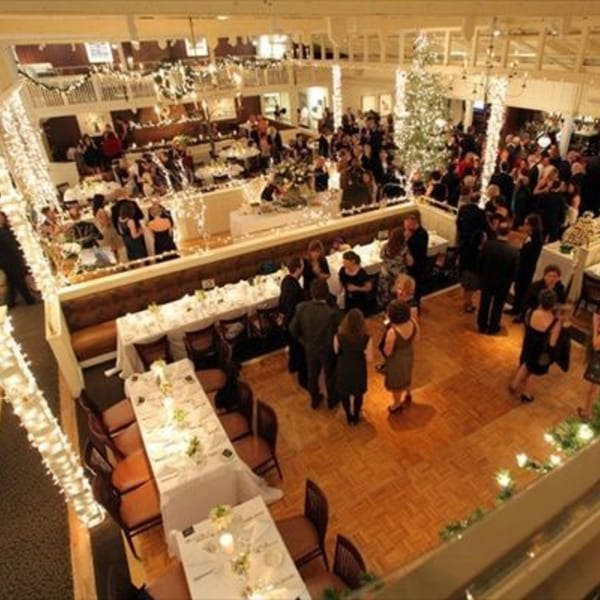 Overhead view of a large, festive event space with people mingling, decorated with string lights and a Christmas tree.