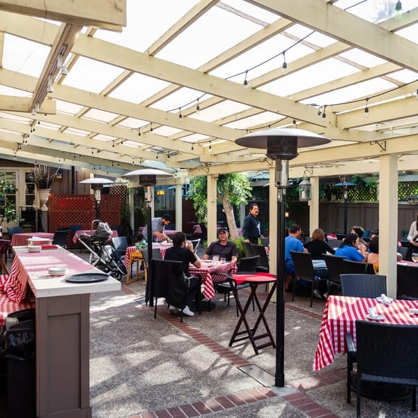 Outdoor patio dining area at MacArthur Park Restaurant with checkered tablecloths, string lights, and patrons.