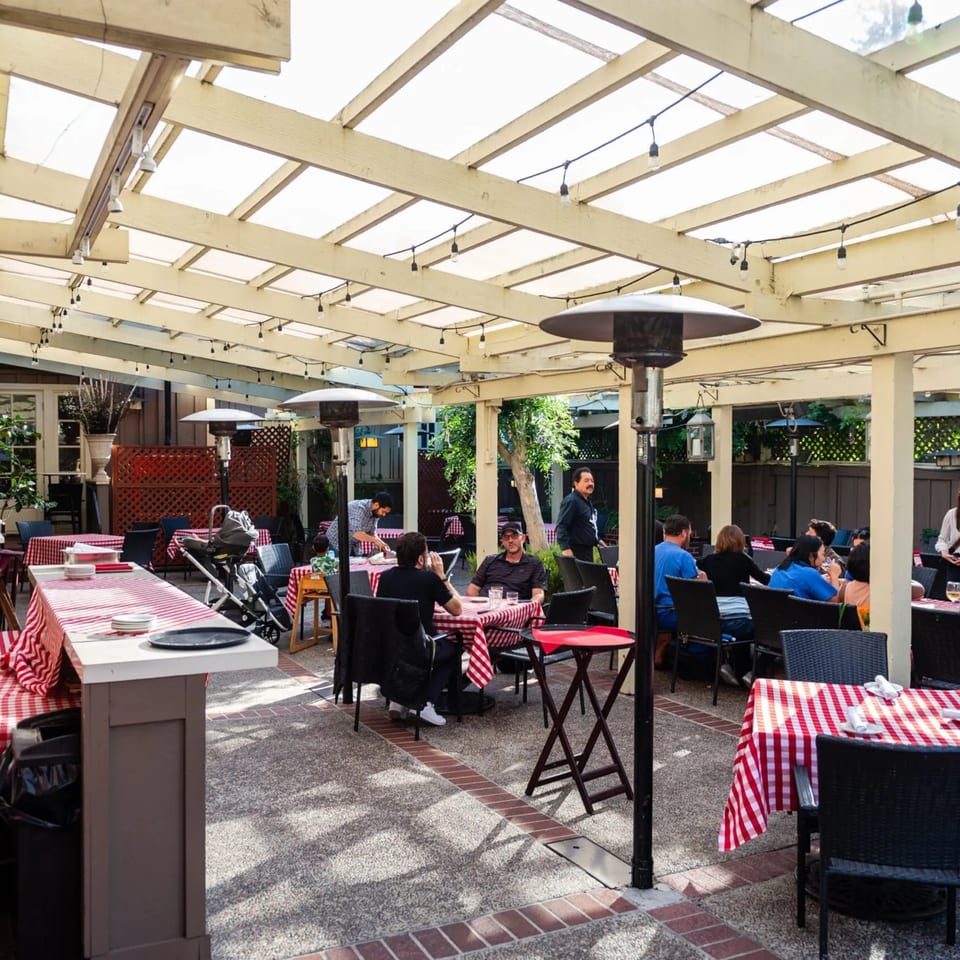 Outdoor patio dining area at MacArthur Park Restaurant with checkered tablecloths, string lights, and patrons.