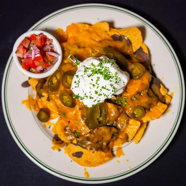 A plate of nachos with melted cheese, jalapeños, sour cream, and a side of pico de gallo.