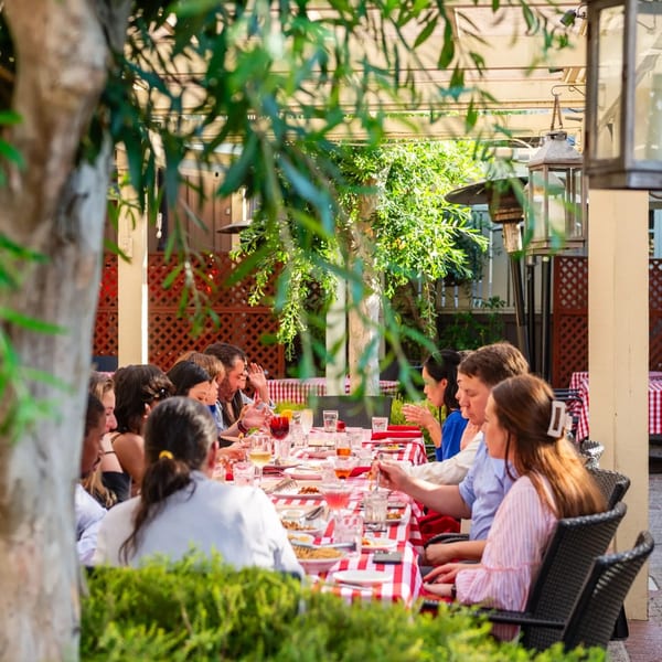 Patrons dining outdoors at MacArthur Park Restaurant, seated at a long table with red and white checkered tablecloths.