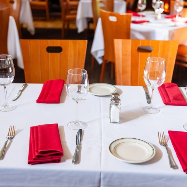 Set tables with white tablecloths, red napkins, wine glasses, and cutlery at MacArthur Park Restaurant.