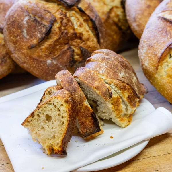 Slices of fresh, crusty sourdough bread on a white plate with whole loaves in the background.